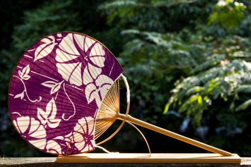 Japanese fan, made of purple kimono cloth, resting in a wooden stand