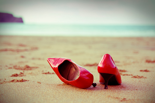 Red shoes in the beach. Cross processing filter added. The shoes are at front and the sea is out of focus at background. The camera is situated in a low position to get the whole picture.