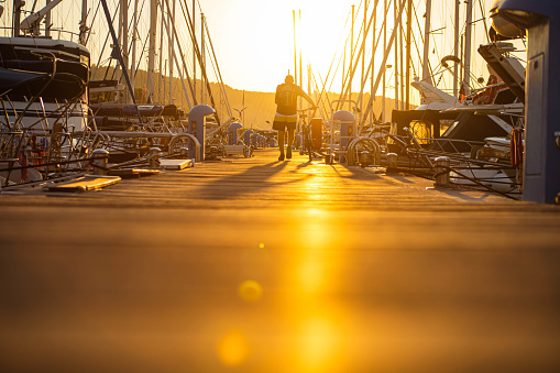 Rearview of active senior men, pushing his bike, in the marina during majestic sunset, while observing the luxury moored yachts and sailboats