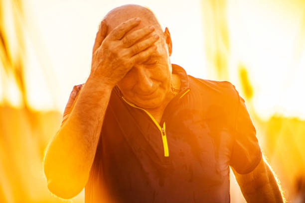 Tired senior man, wiping the sweat from the forehead, while taking a break from jogging at the marina during sunset