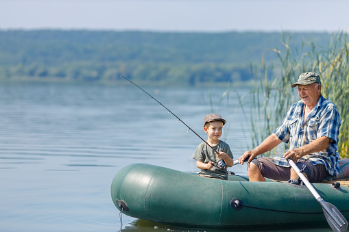 grandfather with grandson together fishing from inflatable boat on the river. Concept of summer family weekend