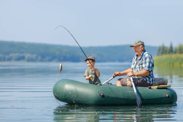 grand-père avec petit-fils ensemble pêchant à partir d’un bateau pneumatique - fishing lake grandfather grandson photos et images de collection