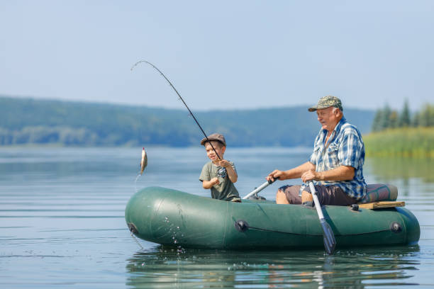 grandfather with grandson together fishing from inflatable boat stock photo