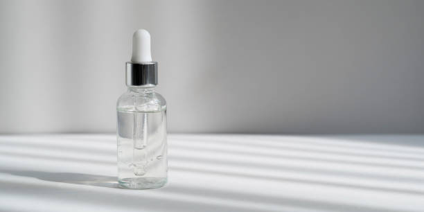 istock Facial serum in transparent glass dropper bottle with stripped hard shadows. Moisturising cosmetic product with pipette on grey background web banner. Skin care gel with collagen and peptides 1340210950