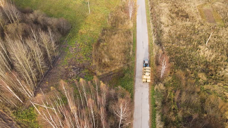 On a country road, a tractor loaded with bales of hay, aerial view.