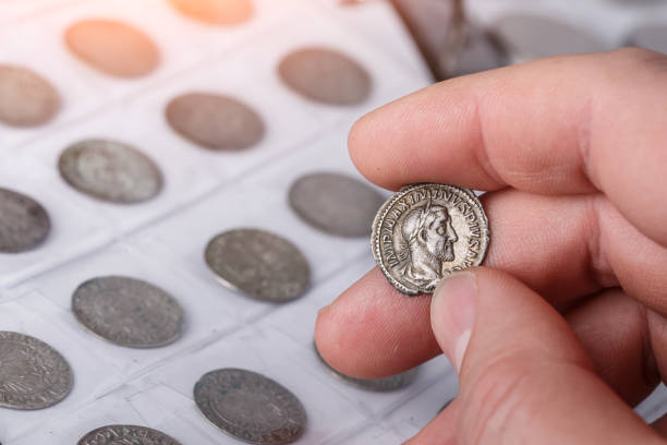 numismatik. alte sammlermünzen aus silber auf einem holztisch. ein sammler hält eine alte münze. antike münze des römischen reiches. - coin collection stock-fotos und bilder