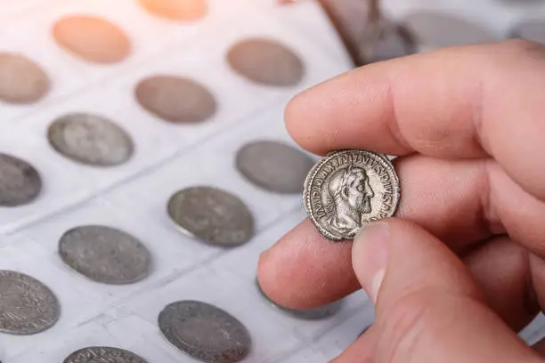 Photo of Numismatics. Old collectible coins made of silver on a wooden table. A collector holds an old coin.Ancient coin of the Roman Empire.