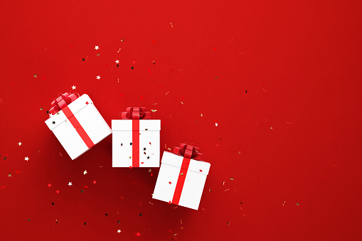 Gold colored confetti falling over white gift boxes on red background. Horizontal composition with copy space. Directly above. Great use for Christmas concepts.