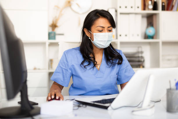 istock Female physician in protective mask filling up medical forms on laptop 1340218421
