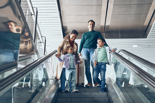 Happy family with two little kids moving by escalator in airport terminal