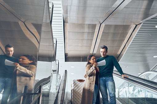 Mature couple carrying tickets while moving by escalator in airport terminal