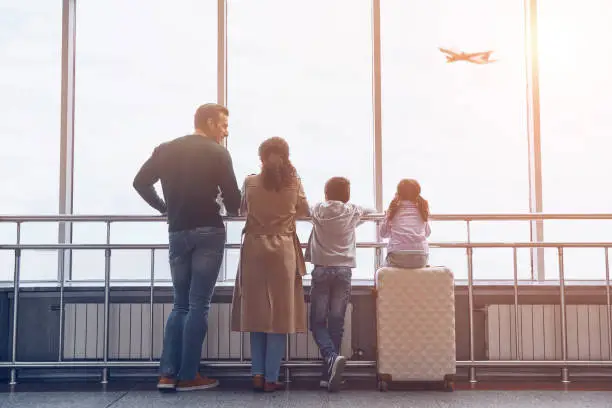 Photo of Full length of family with two little kids looking at the flying airplane