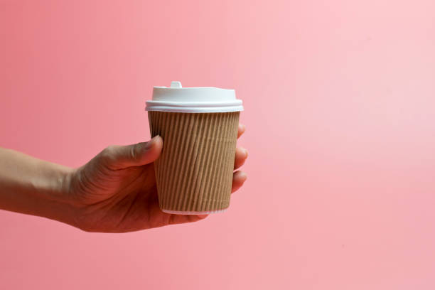 Hand Holding A Paper Cup Against Pink Background stock photo