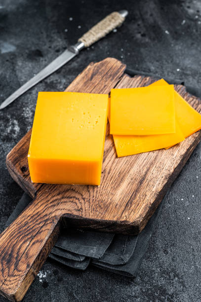 Slices of Cheddar Cheese on a wooden cutting board. black background. Top view Slices of Cheddar Cheese on a wooden cutting board. black background. Top view. cheddar cheese stock pictures, royalty-free photos & images
