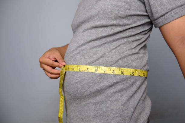 homem asiático vestindo camisa cinza medindo sua cintura com fita de medição cintura amarela - overweight dieting men unhealthy eating - fotografias e filmes do acervo