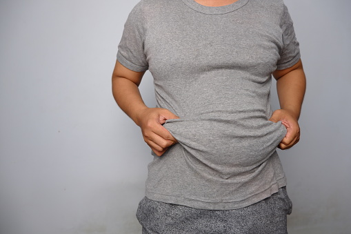Asian man wearing grey shirt holding and lifting his fat flabby belly