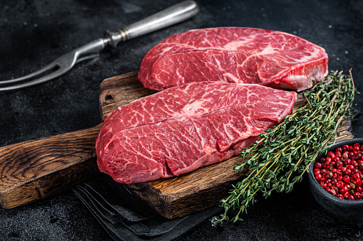 Fresh Raw Top Blade or flat iron beef meat steaks on a butcher cutting board. Black background. Top View.