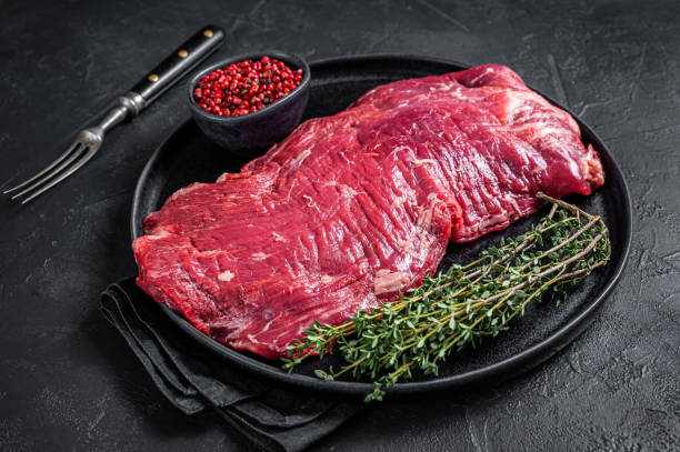 istock Flank or flap raw beef steak on plate with thyme. Black background. Top view 1340228746
