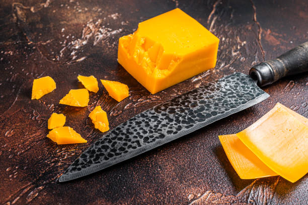 istock Cheddar Cheese sliced on a kitchen table with knife. dark background. Top view 1340228977