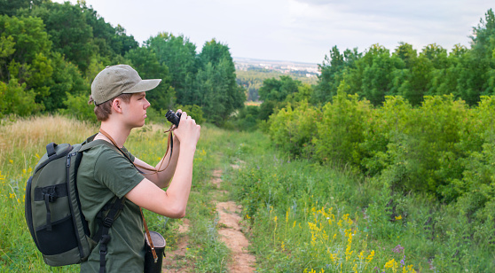 Teenager boy hiking. Teen looking through binoculars into the distance near the forest.