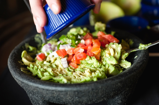 woman pouring diced tomatoes and onions over a guacamole