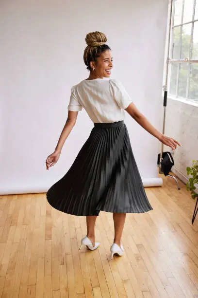 Rear view of a smiling young African American woman twirling a long skirt in front of a white backdrop