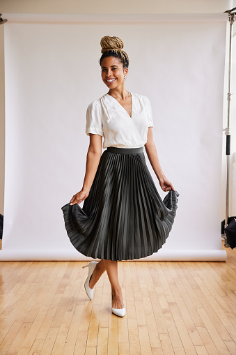 Portrait of a smiling young African American woman in a long skirt curtseying in front of a white backdrop