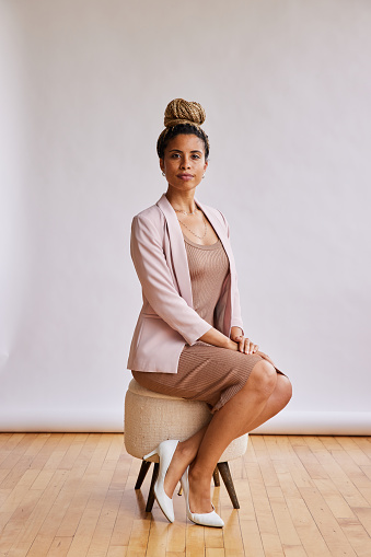 Portrait of a confident young African American businesswoman sitting on a stool in front of a light backdrop