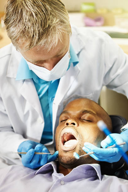 istock Dentist examining a patient reclining with open mouth in the surgery 1340245568
