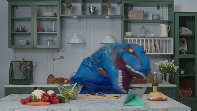 Big blue dinosaur dancing positive in kitchen. Comical movements of person in dino mascot. Positive mood at home.