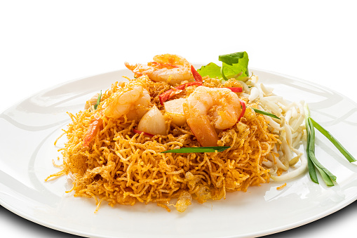 Closeup view of homemade crispy fried rice noodles with shrimp, bean sprout and garlic in white ceramic plate isolated on white background with clipping path.