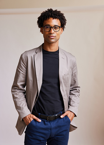 Portrait of a confident young African American businessman standing with his hands in his pockets against a gray background