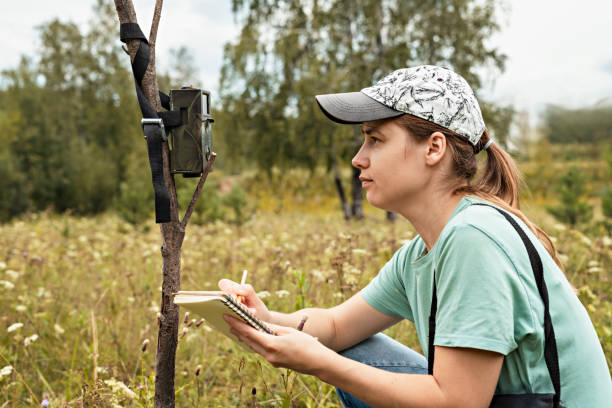 istock Young woman scientist zoologist writing down data from trap camera to notepad, observing wild animals in reserve taiga forest, monitoring of rare endangered animal species, World Wildlife Day 1340259857