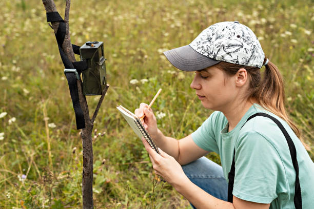 istock Young woman scientist zoologist writing down data from trap camera to notepad, observing wild animals in reserve taiga forest, monitoring of rare endangered animal species, World Wildlife Day 1340259859