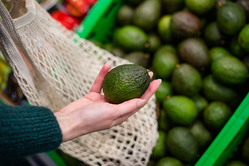 Woman choosing avocados in the supermarket. Close up of hand holding avocado in farm market.