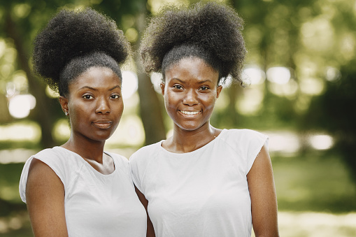 A young female african-american women enjoying a day at the park. Teenagers wearing white t-shirt. Sisters posing for a photo.