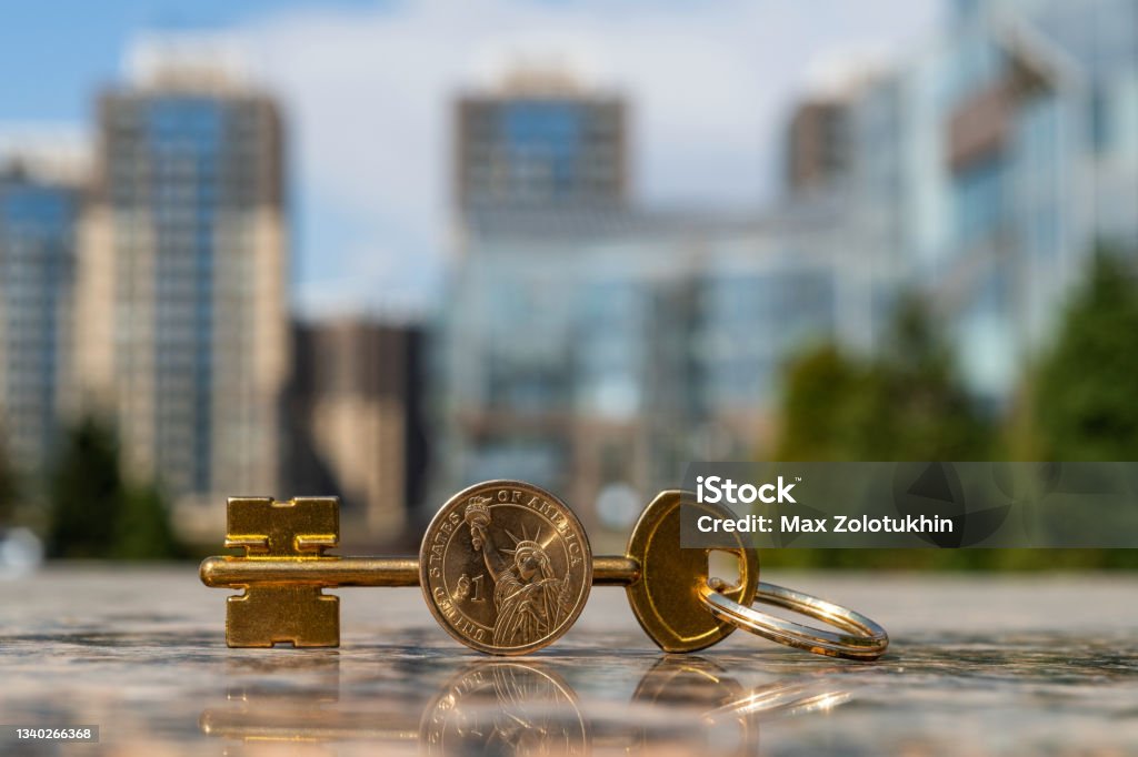 Golden key and 1 american dollar coin on modern buildings background Apartment Stock Photo