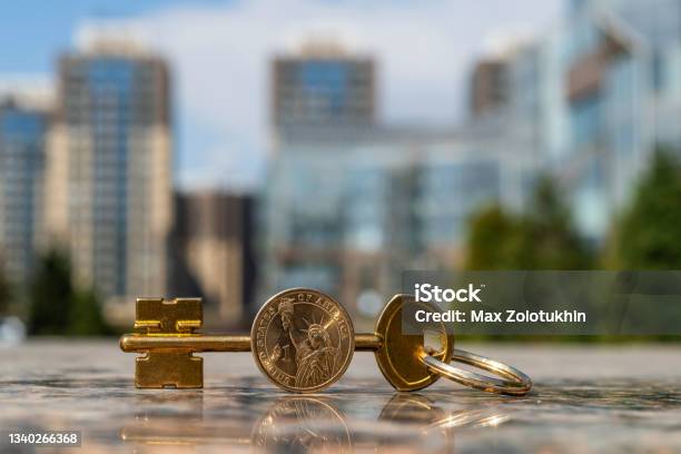 Golden Key And 1 American Dollar Coin On Modern Buildings Background Stock Photo - Download Image Now