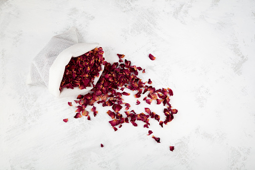 Dried rose petals in pouch, top view. Light background, copy space. Pink colored organic herb used for perfumes, cosmetics, teas and baths. Red dry petals.