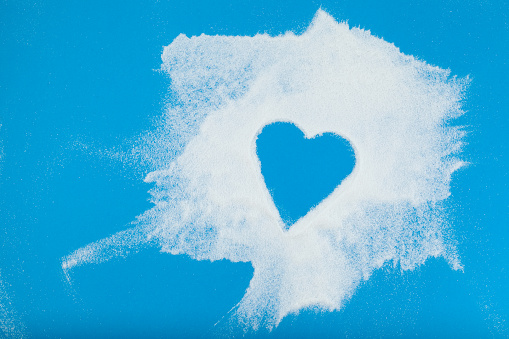 White powder is chaotically scattered on blue surface. Empty space in the form of heart. Collagen or protein. Healthy food Supplement.