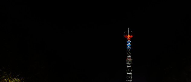 Glowing TV tower at night. Festive illuminated broadcast tower. Space for text.