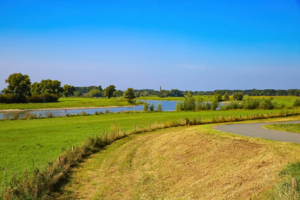 View from cycling track on typical dutch rural landscape with agricultural fields and river Ijssel against blue summer sky View from cycling track on typical dutch rural landscape with agricultural fields and river Ijssel against blue summer sky - between Bronkhorst and Zutphen, Netherlands ijssel photos stock pictures, royalty-free photos & images