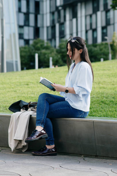 istock Young woman reading a book in a public park 1340275380