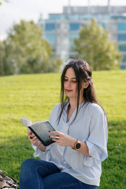 istock Young woman reading a book in a public park 1340275454