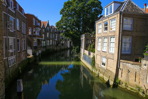 Dordrecht, Netherlands - July 9. 2021: View on water canal with residential houses and green tree against blue summer sky