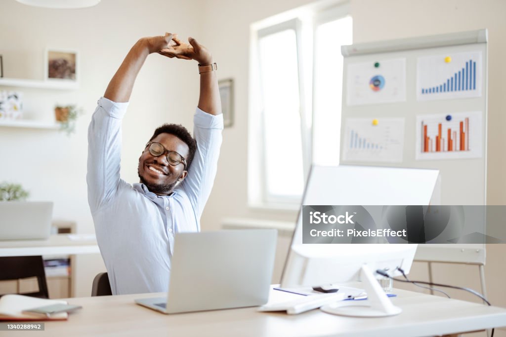 Businessman Stretching His Arms African american man stretching doing easy office exercises to relieve muscle tension from sedentary work, young black employee taking break for relaxation at workplace, computer syndrome prevention Stretching Stock Photo