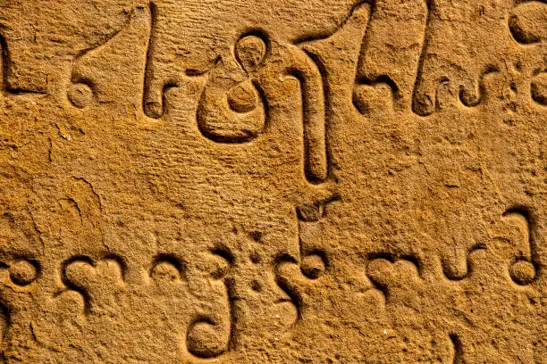 Photo of Close-up Ancient carving of Mkhedruli alphabet developed between the 11th and 13th centuries - official language of Georgia - on old grainy sandstone wall.