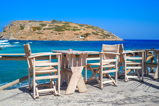 Empty rustic wooden table and chair on terrace at waterfront. Relaxing on seaside, summer vacation at sea concept. Crete, Greece.