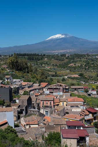 Small houses in village in countryside. Snowcapped famous Etna volcano in distance. Clear blue sky. Sicily, Italy.