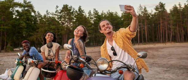 istock Happy young people, motorcycle riders smiling while taking a selfie together, sitting on scooters outside the city 1340294454